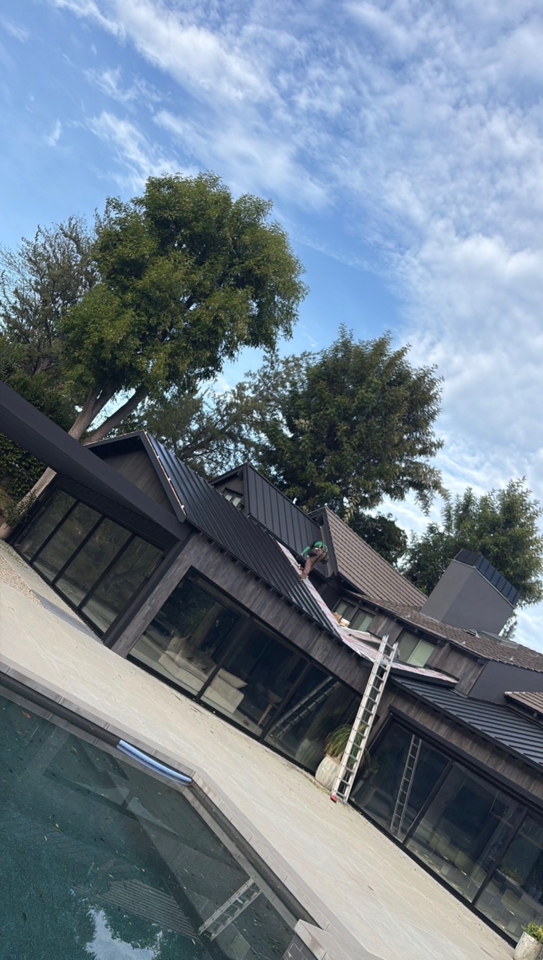 Installer setting dark standing seam metal panels on a poolside residence in San Diego County