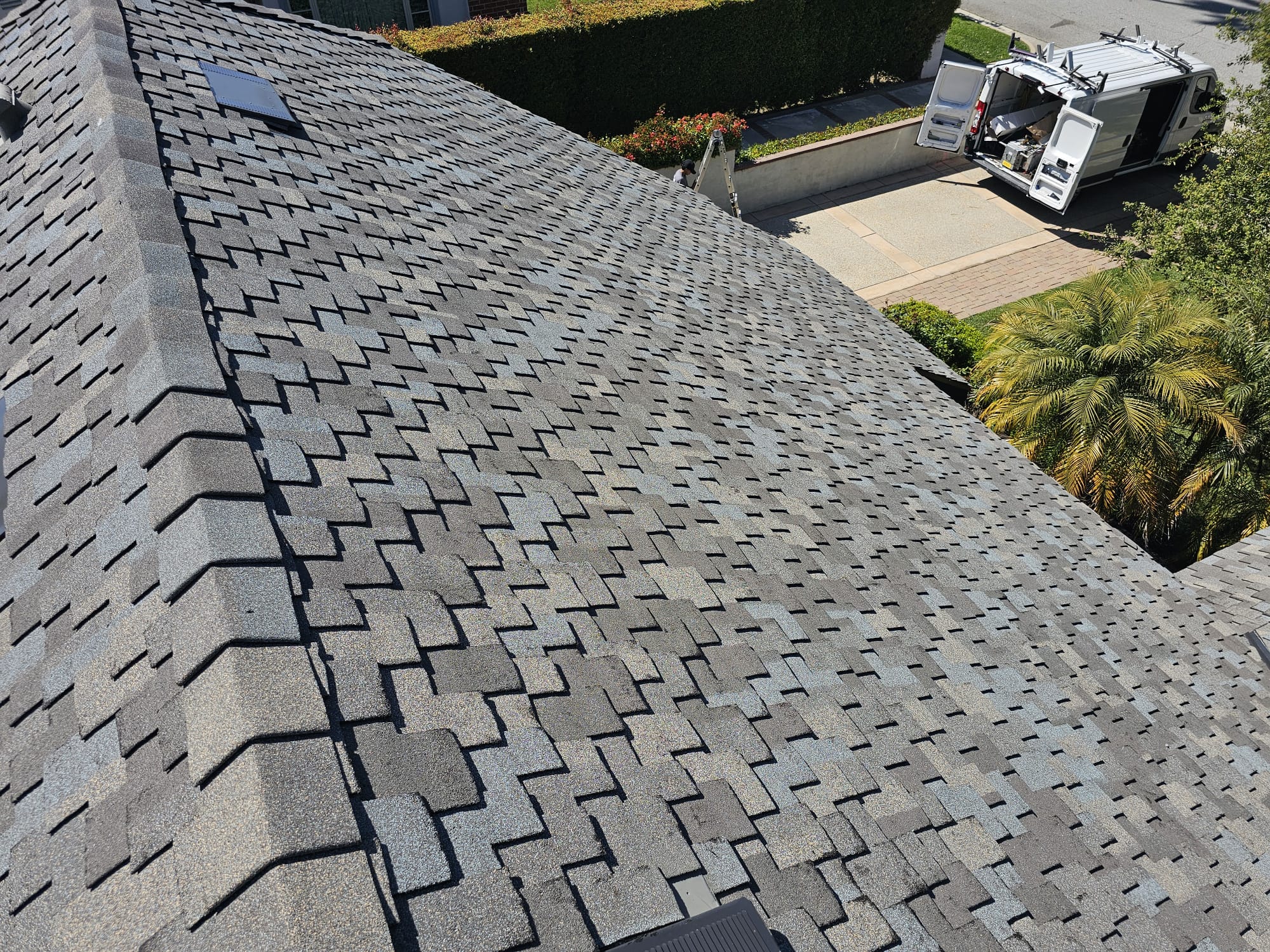 Close aerial view of a new gray shingle hip roof with metal pipe flashing
