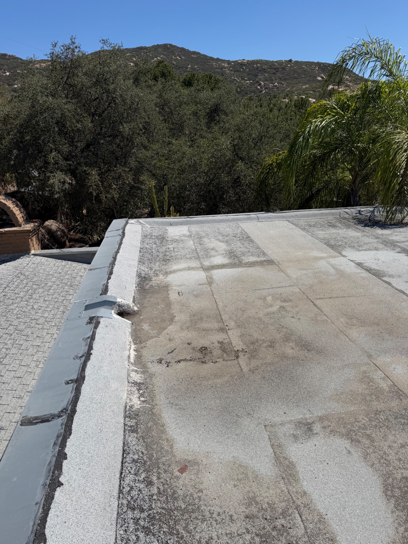 Cap sheet flat roof section with ponding stains and worn granules next to a shingle roof
