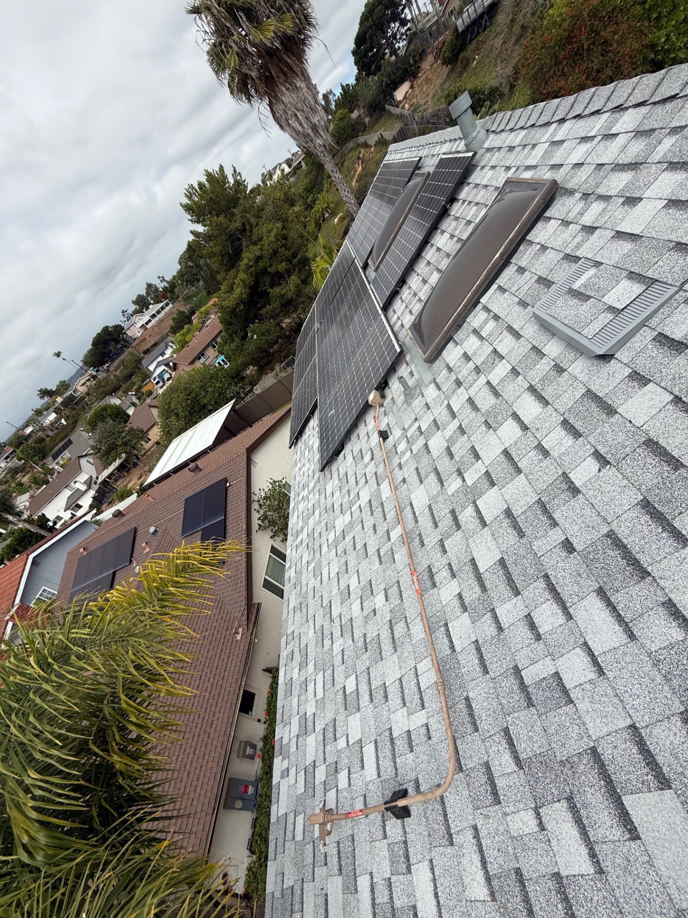 Completed gray architectural shingle roof with solar panels, skylights, and new roof vents