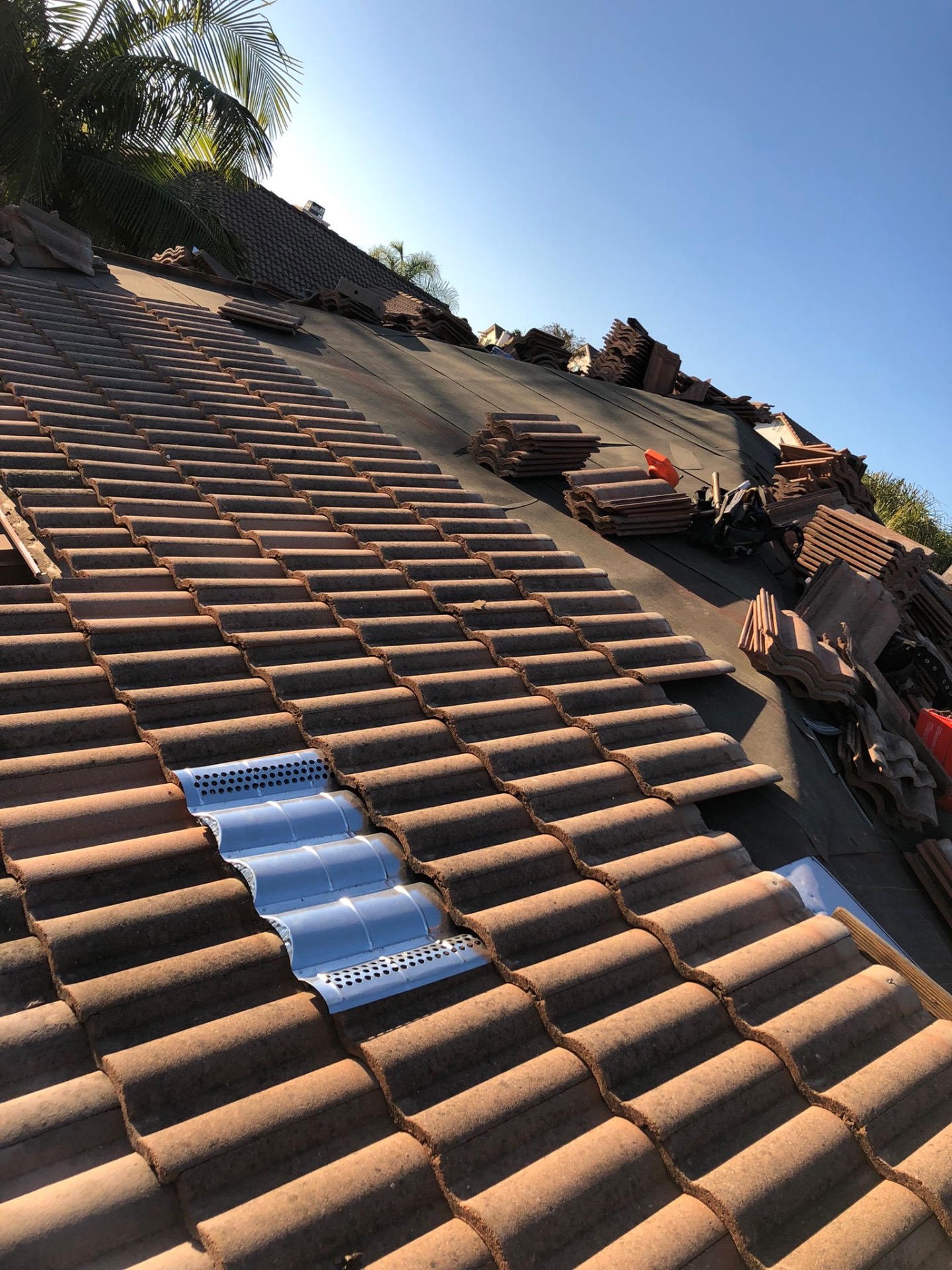 S-tile roof being relaid over new underlayment with metal O'Hagin attic vents in San Diego