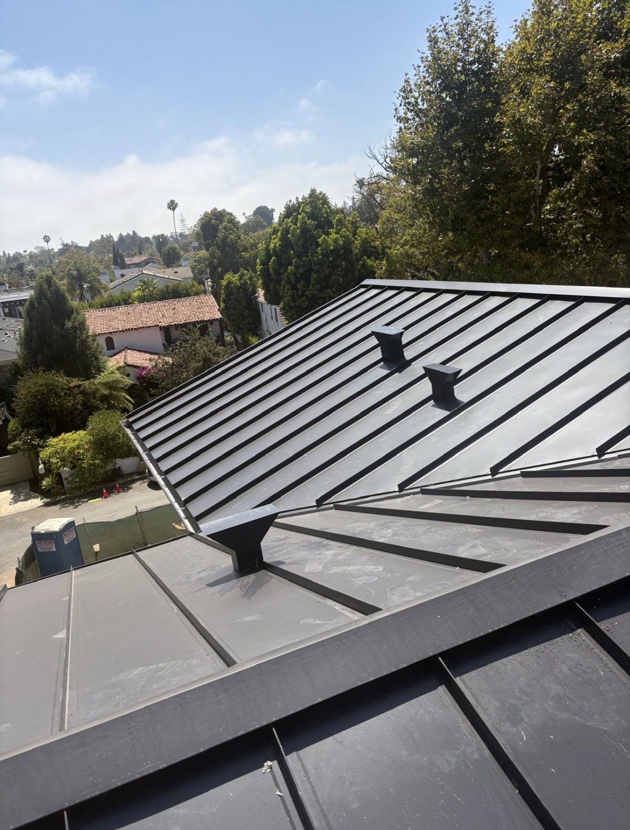 Standing seam metal roof planes meeting at a ridge with black roof jacks and vents installed