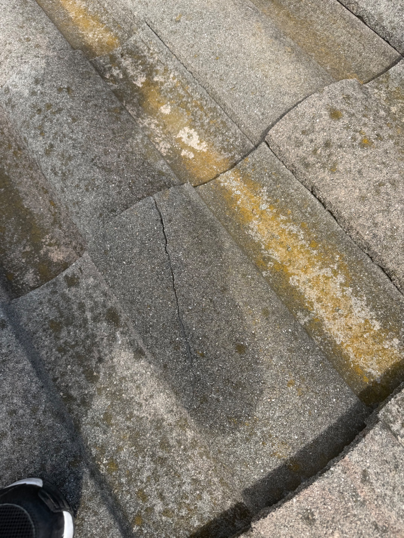 Cracked concrete roof tiles with moss and lichen growth on a San Diego roof