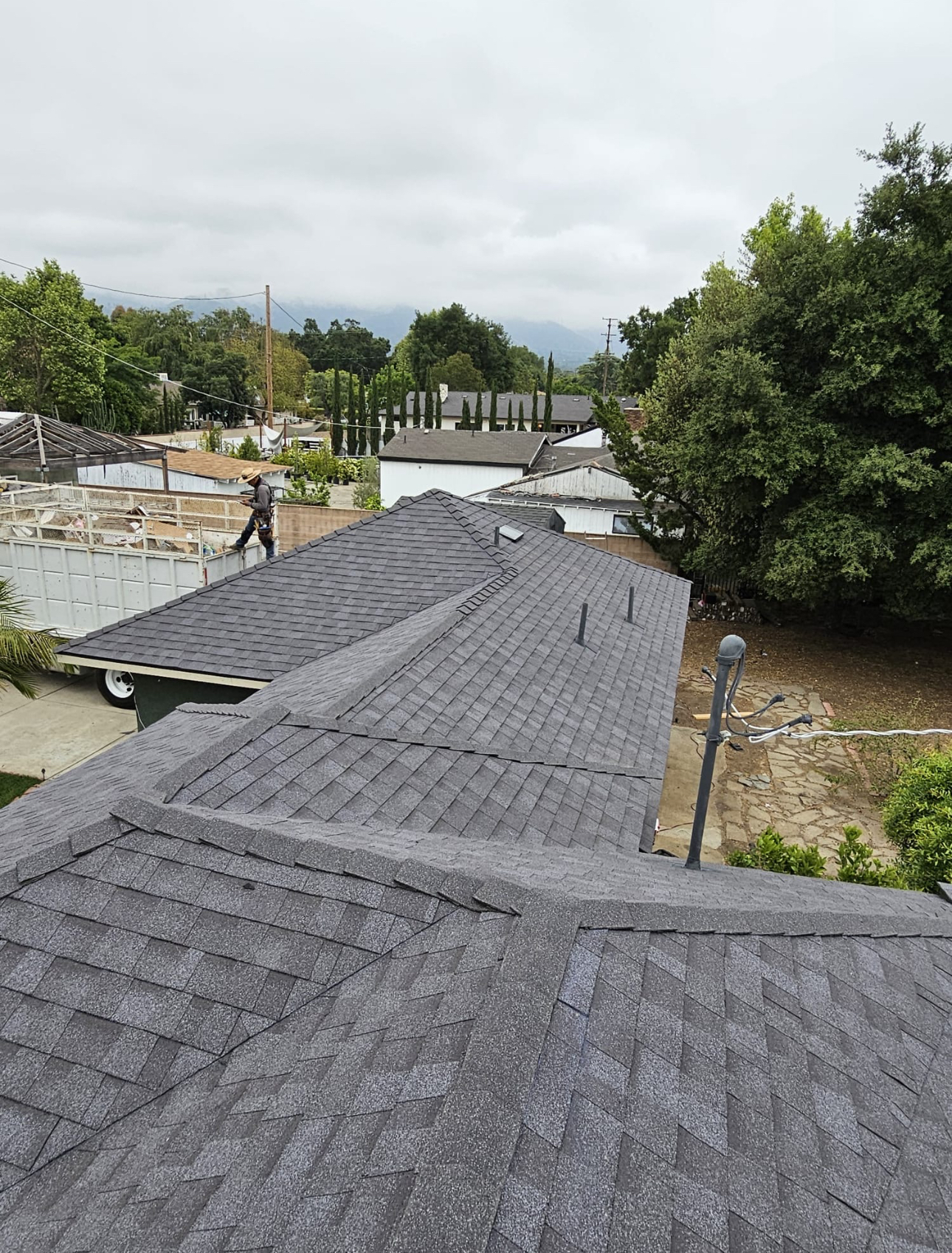 Overview of a completed gray shingle roof with garage and dump trailer staged below