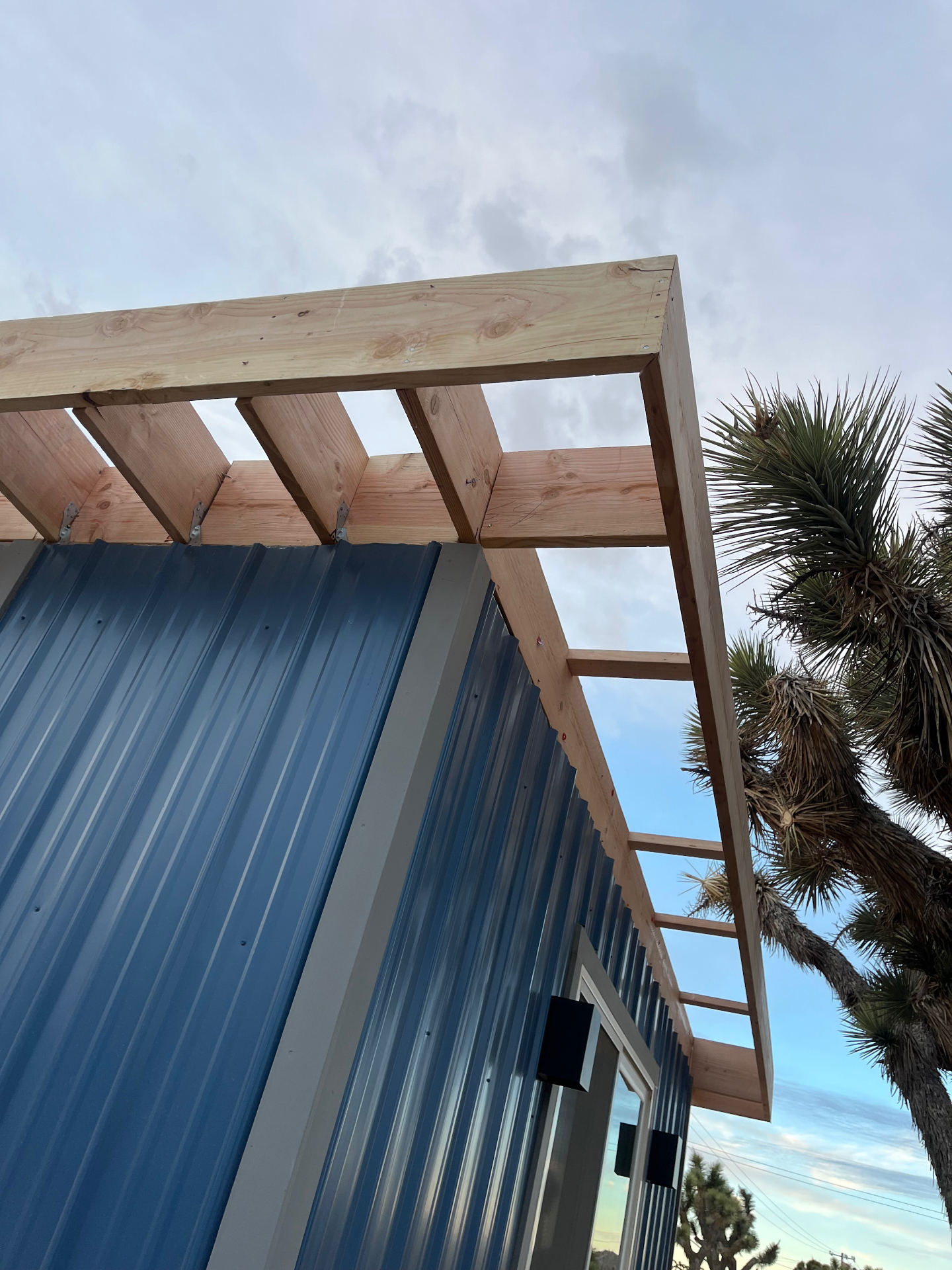 New wood patio cover framing with rafters and outlookers tied into a metal-clad building