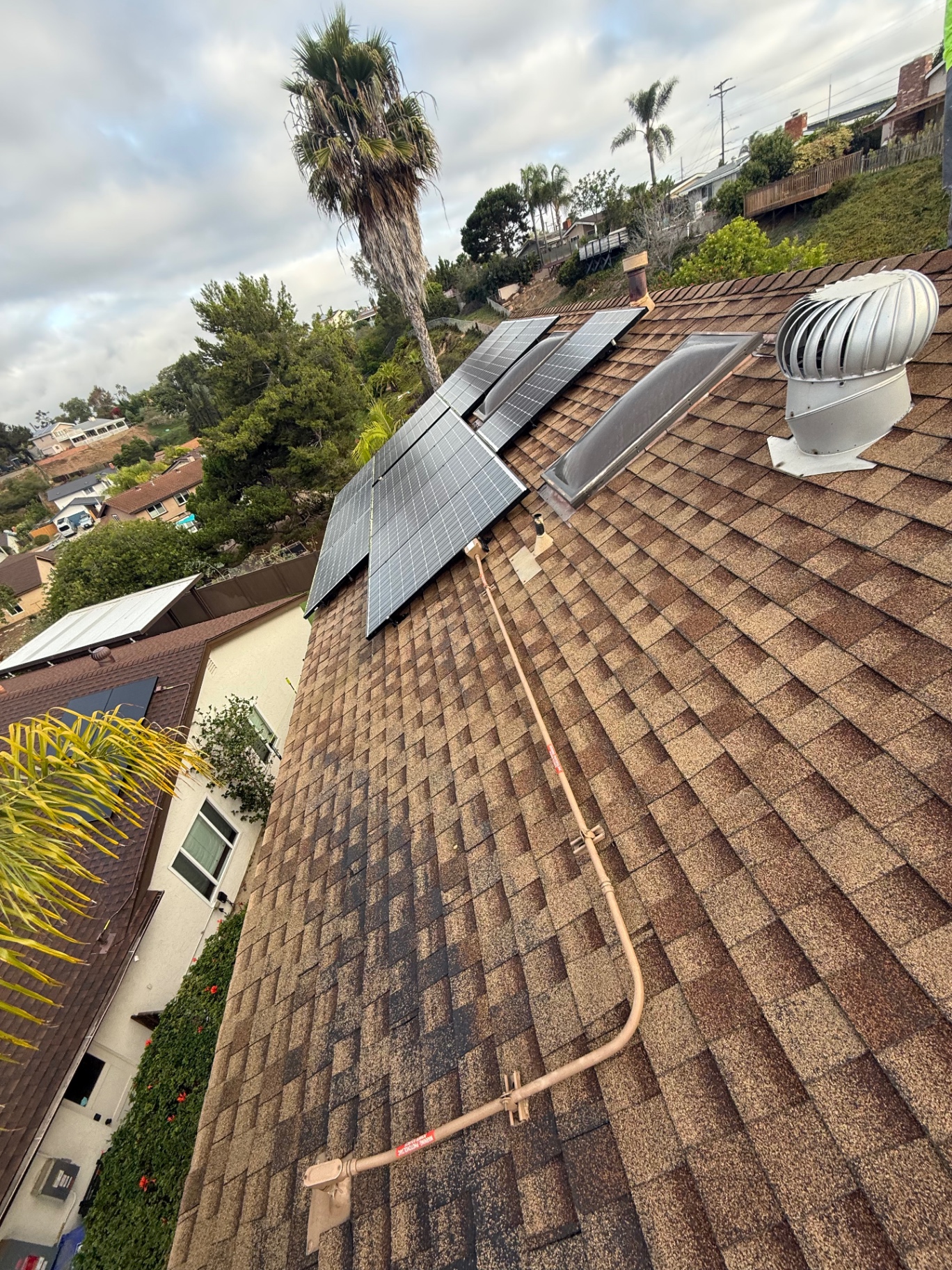 Aged brown asphalt shingle roof with solar panels before complete replacement in San Diego