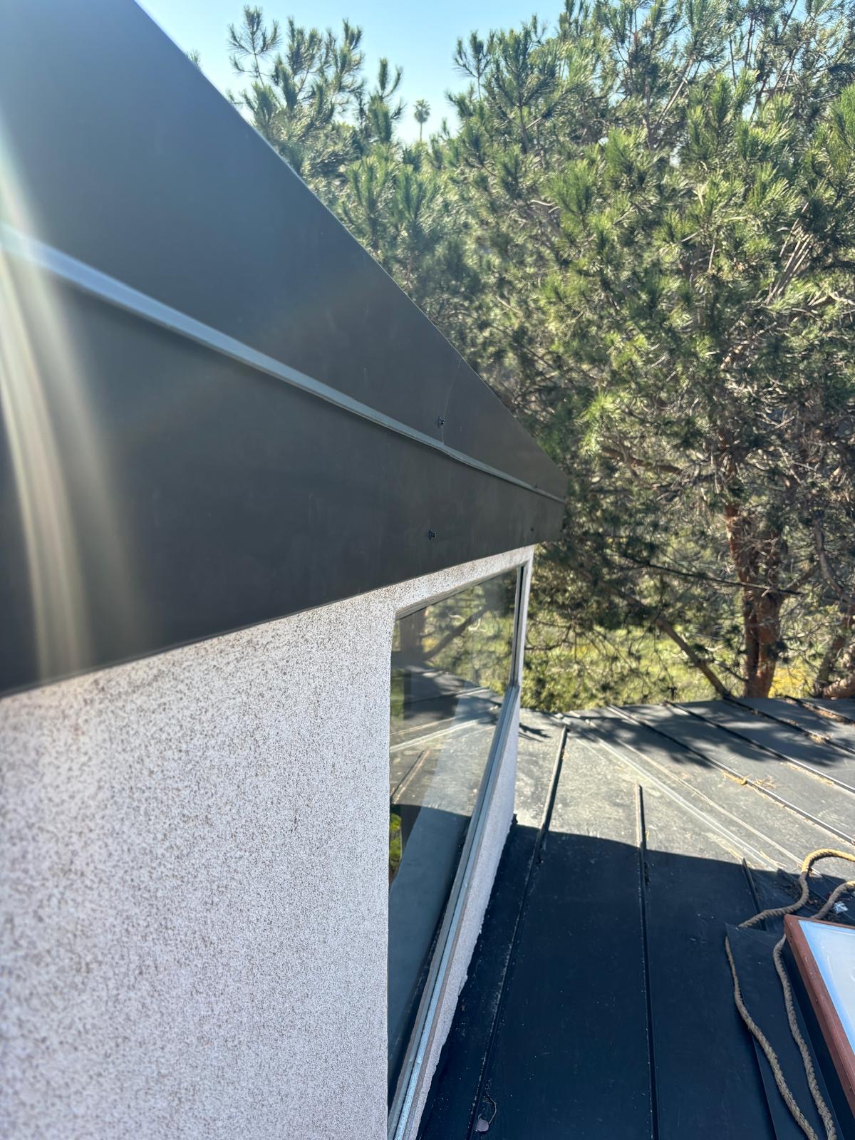 Metal fascia board running along a stucco wall beside a standing seam metal roof