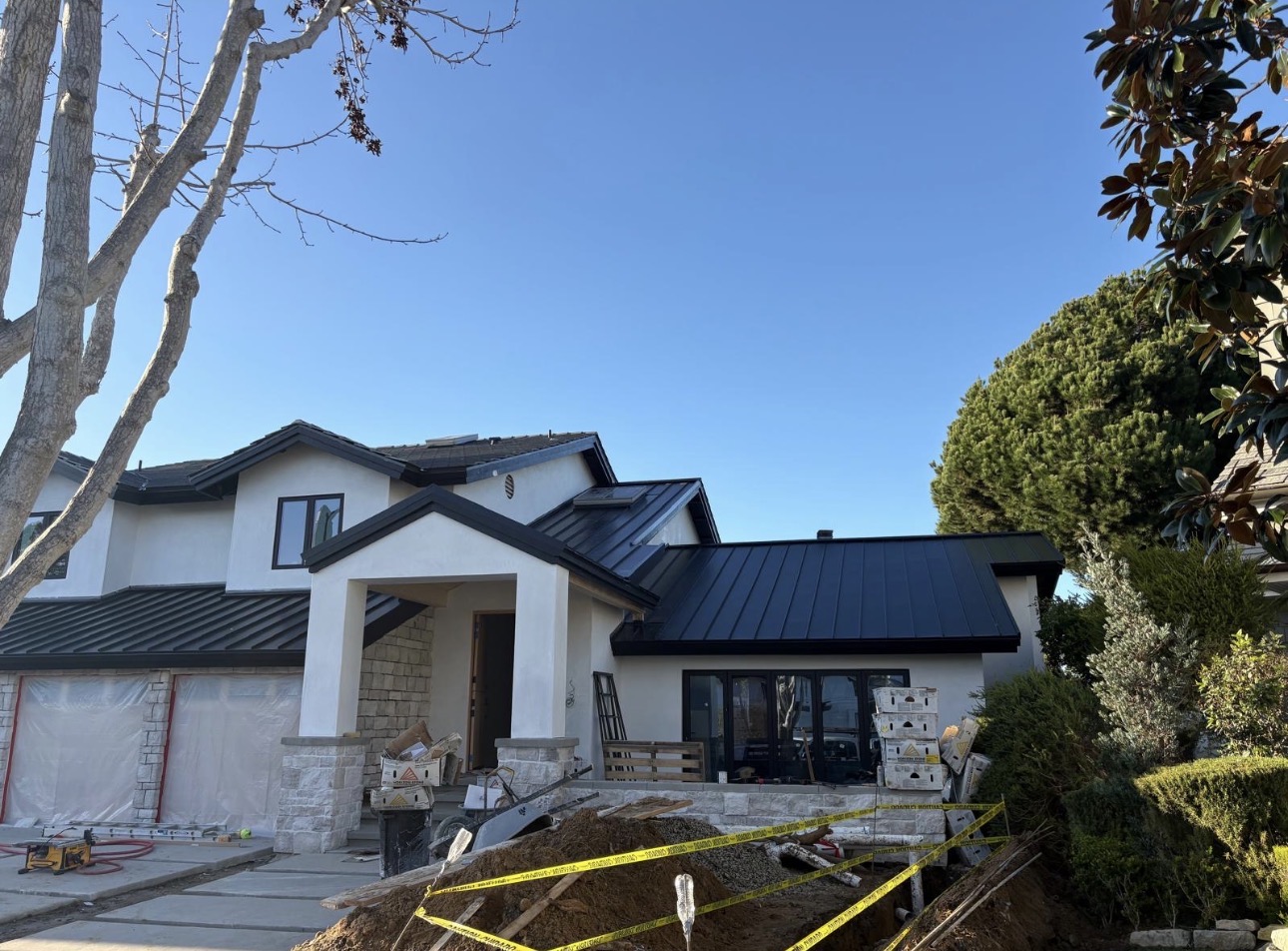 Completed matte black standing seam metal roof on a two-story stucco and stone home