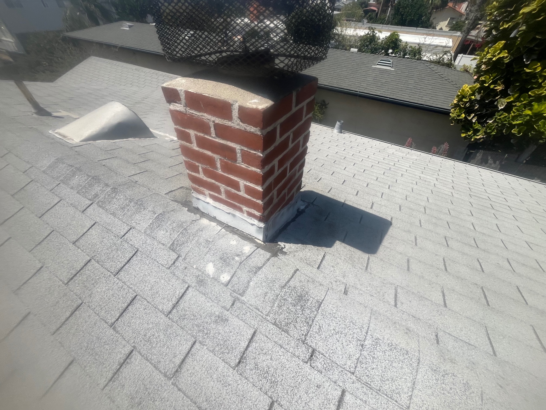 Chimney flashing patched with roof mastic on a composition shingle roof in San Diego