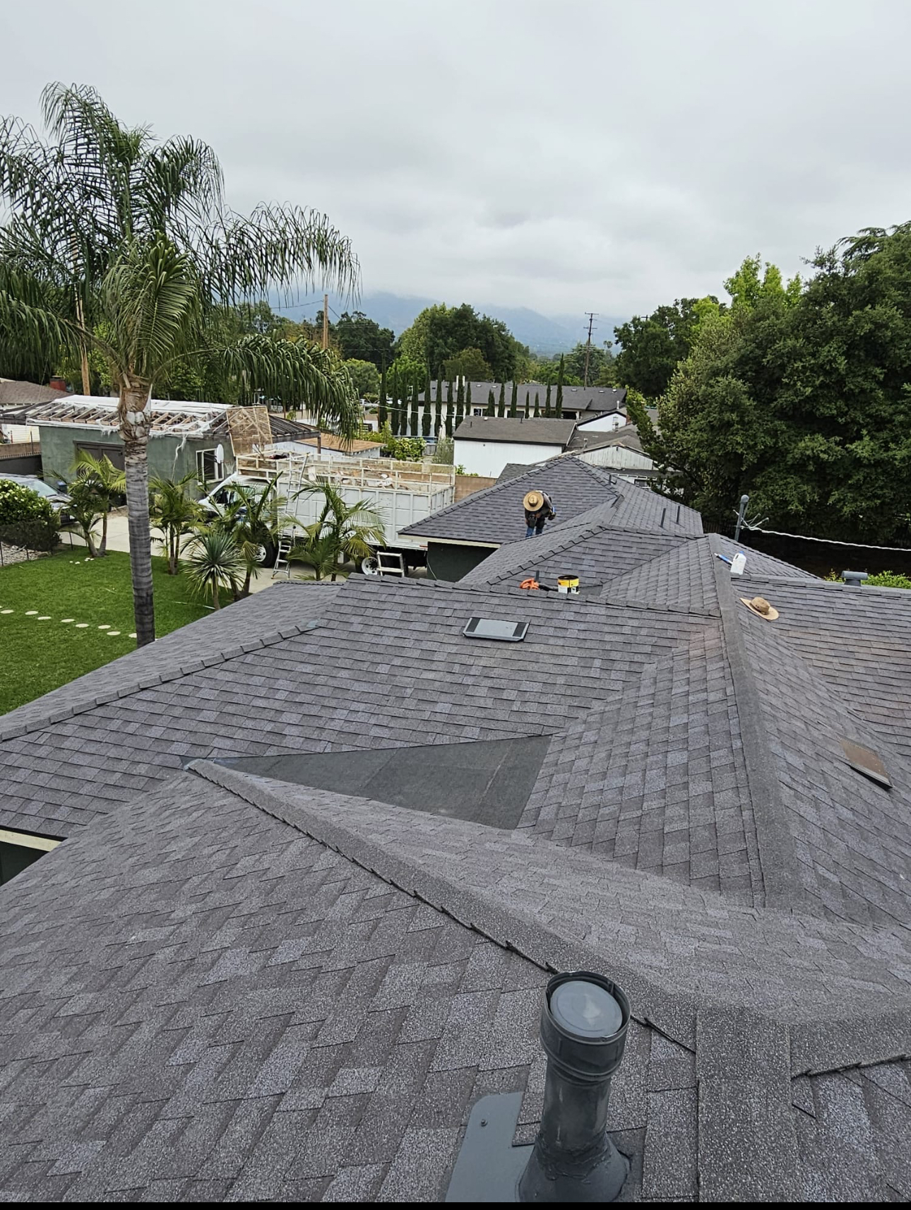Installer working on a large multi-hip gray shingle roof replacement