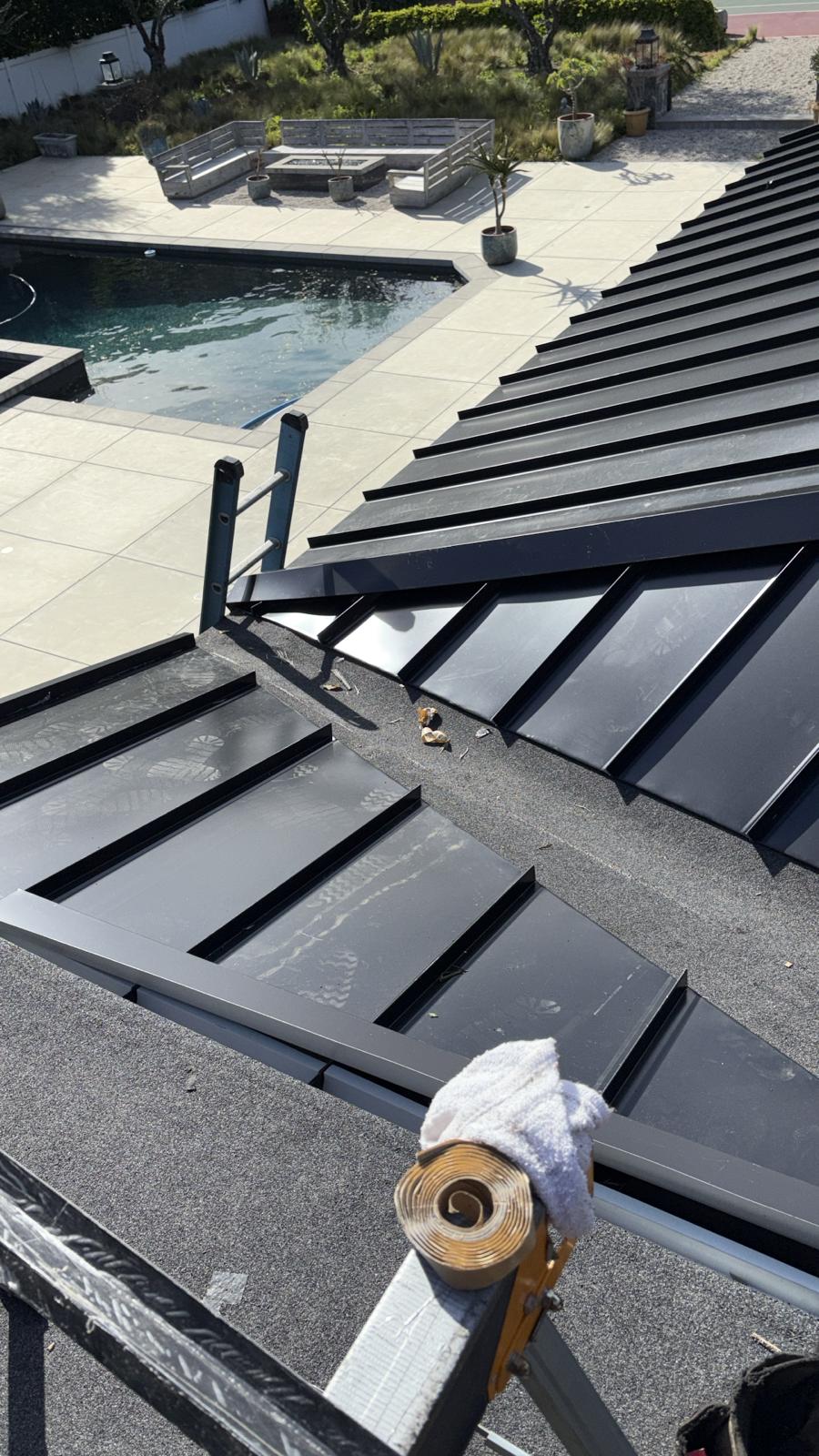 Completed matte black standing seam metal roof overlooking a pool and firepit patio in San Diego County