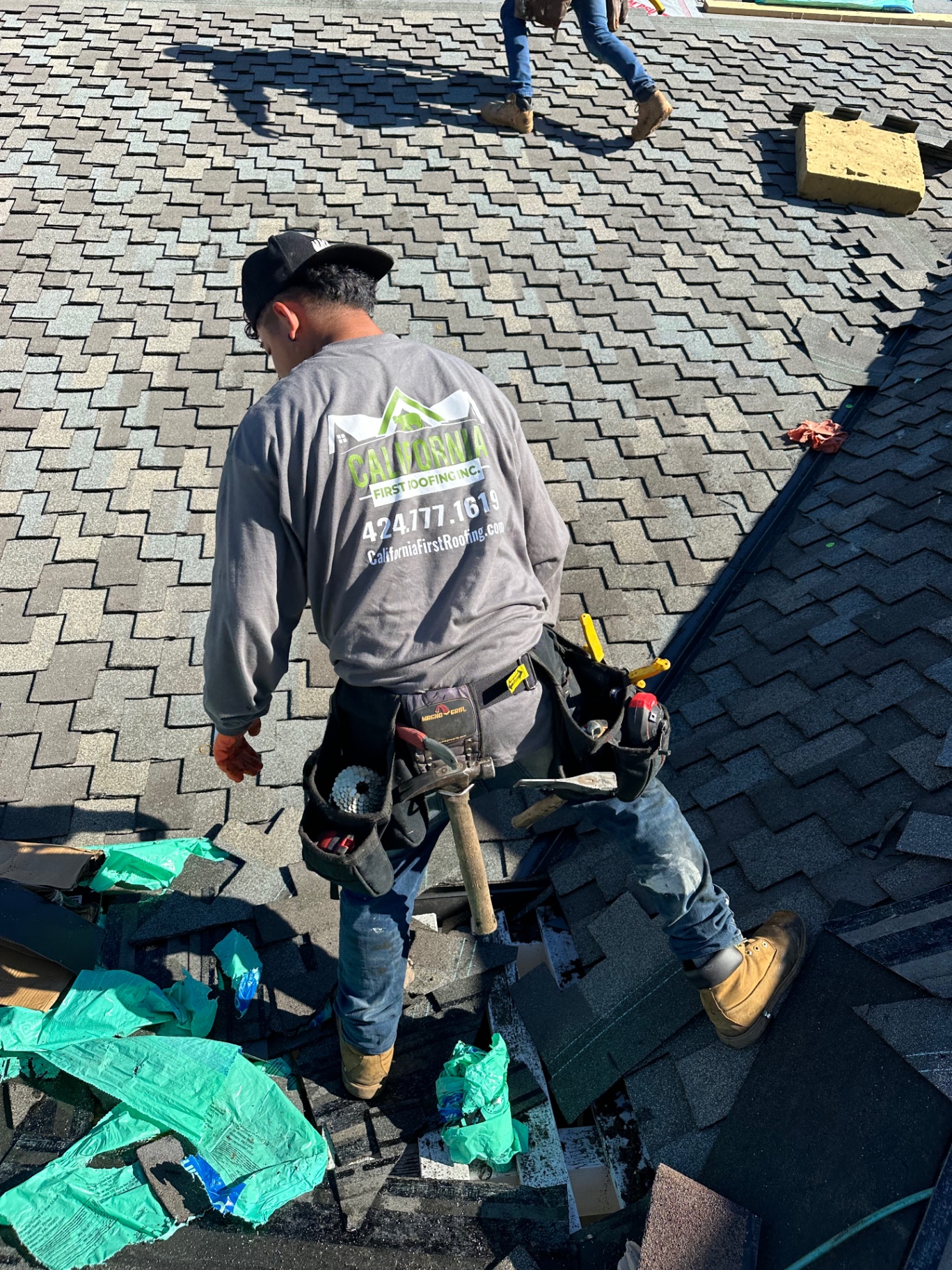 California First Roofing installer with tool belt walking a residential shingle roof during a tear-off and re-roof in San Diego