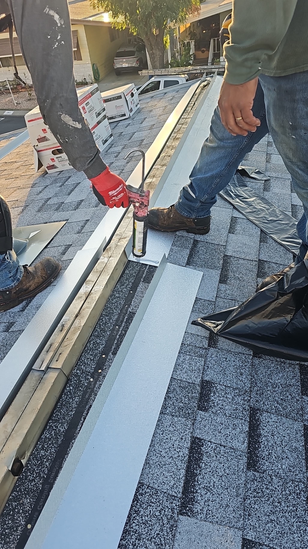 Roofer sealing metal ridge vent seams with sealant on a San Diego shingle roof