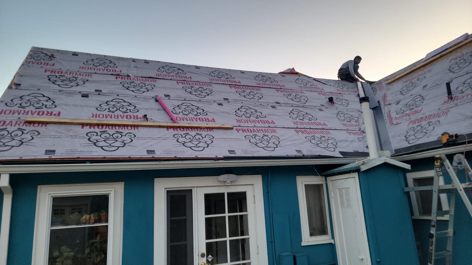 Roofer installing ProArmor synthetic underlayment over new plywood decking on a San Diego home