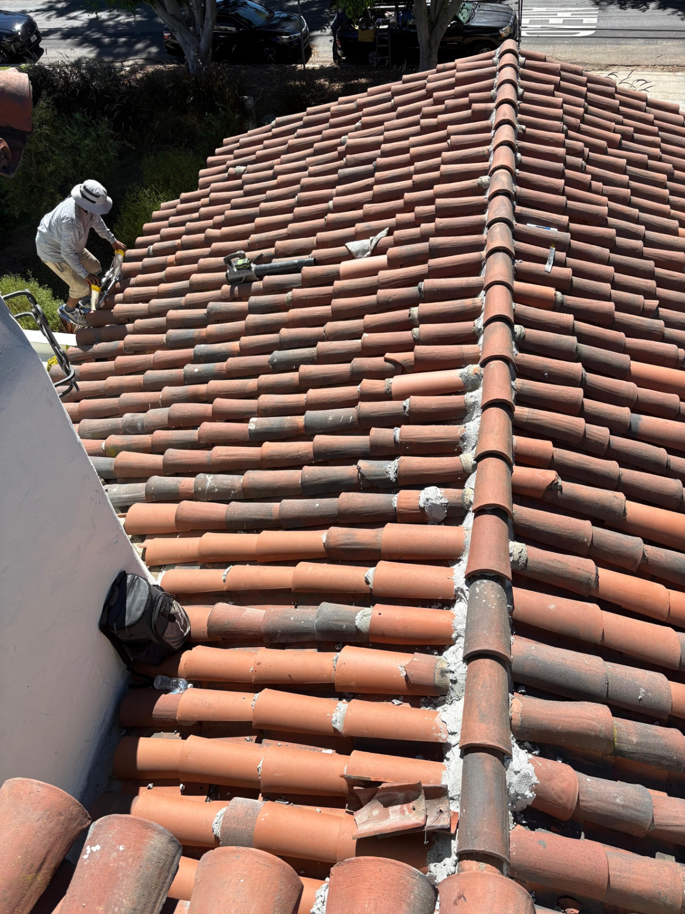 Crew member working on clay tile ridge caps next to a low-slope roof section