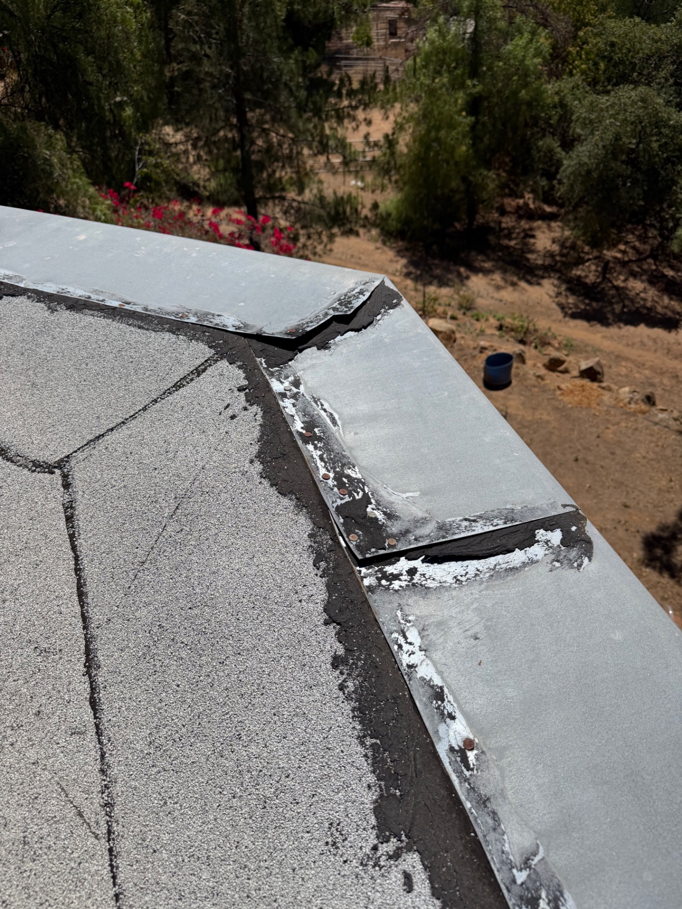 Failed edge metal seam on a cap sheet flat roof patched with tar and exposed nails