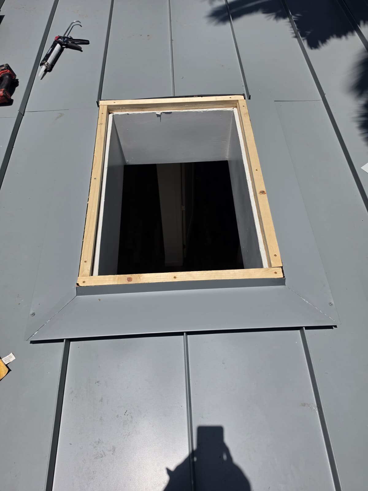 Open skylight curb framed into a gray standing seam metal roof