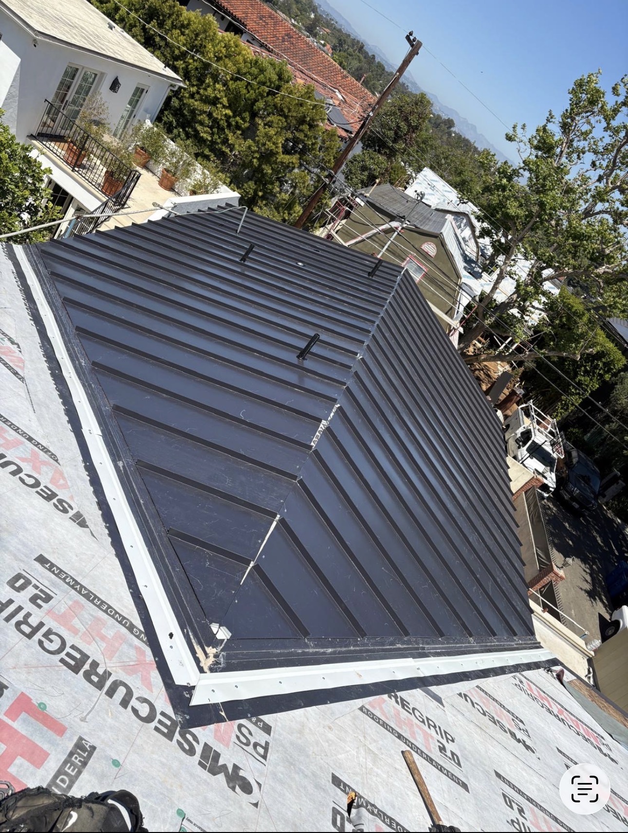 Aerial view of a charcoal standing seam metal hip roof with white drip edge over synthetic underlayment