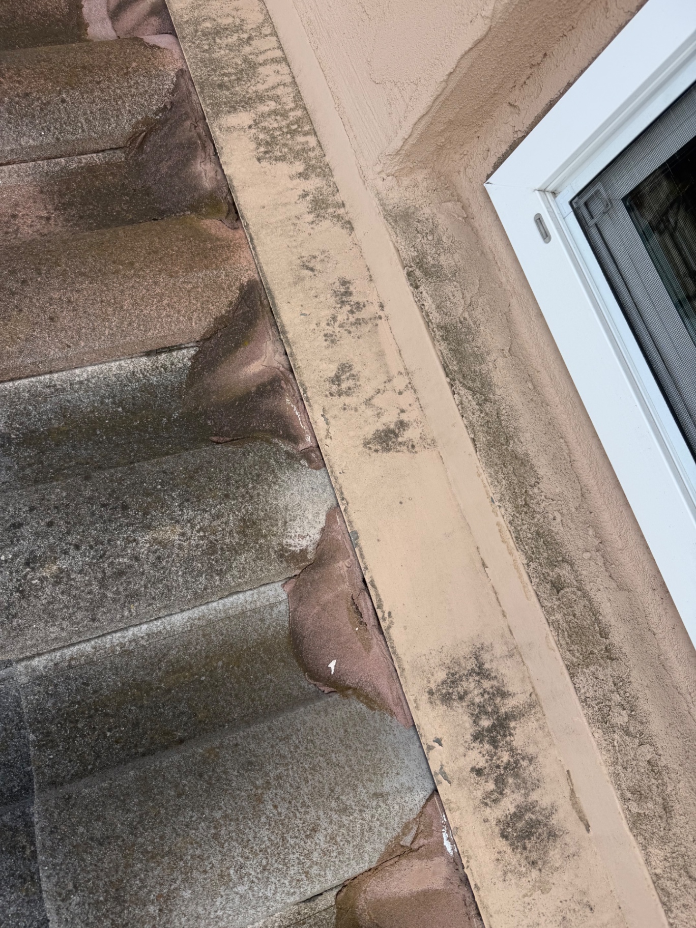 Roof tile to stucco wall termination with failed mortar and mold staining on the wall