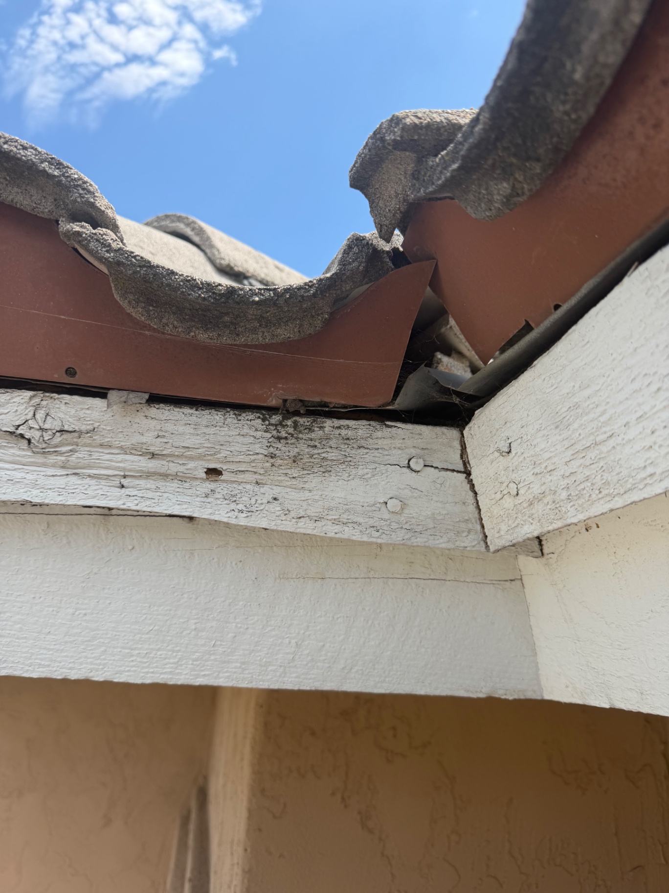 Crushed roof tile at the eave with a gap above deteriorated fascia board