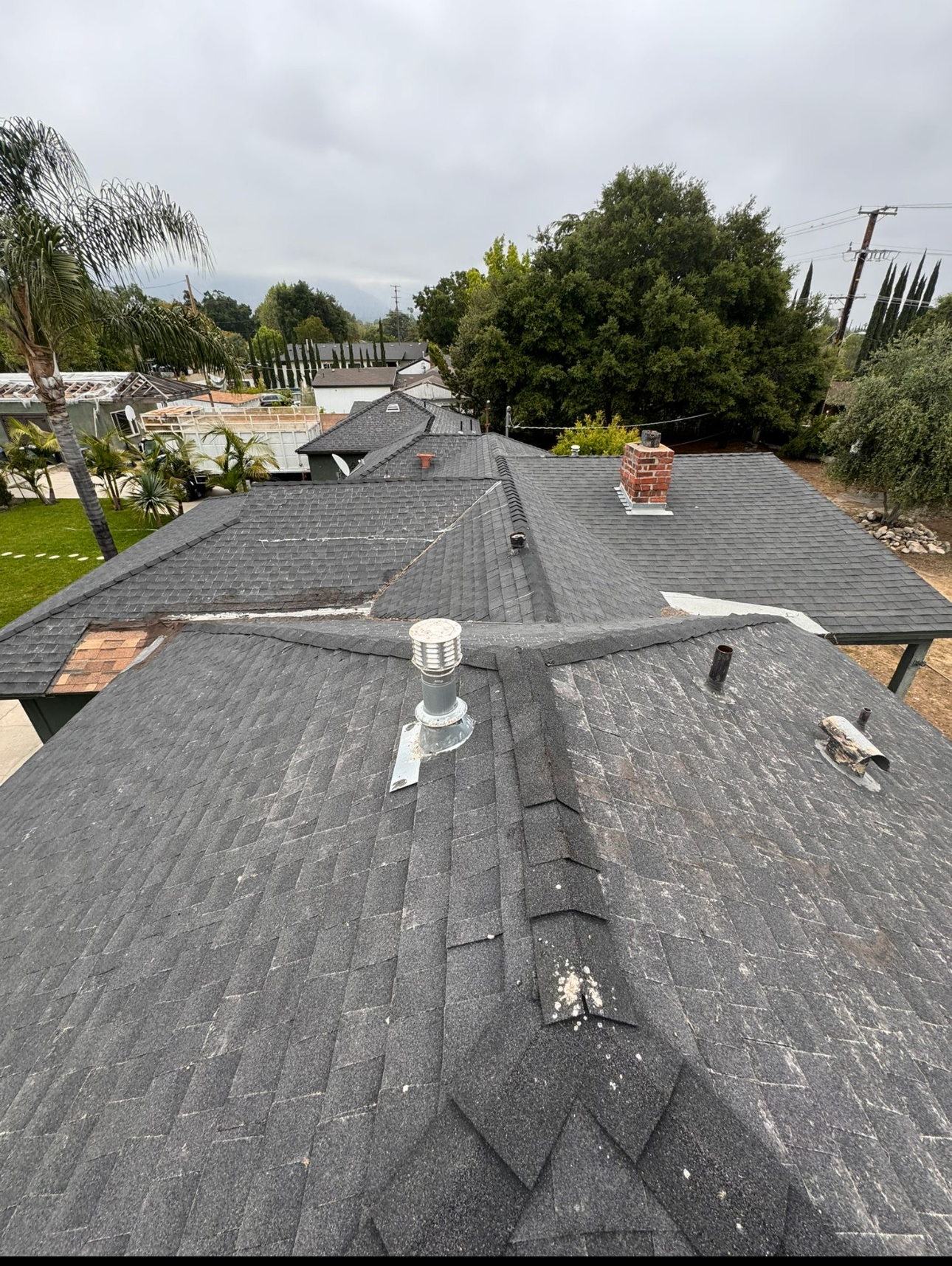 Existing aged shingle roof with brick chimney and vents documented before replacement