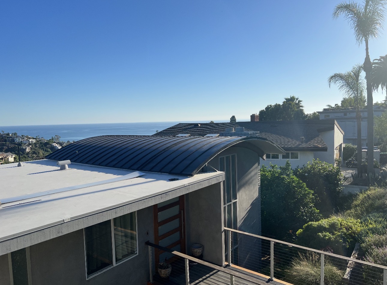 Curved dark bronze standing seam metal roof on a coastal California home overlooking the ocean