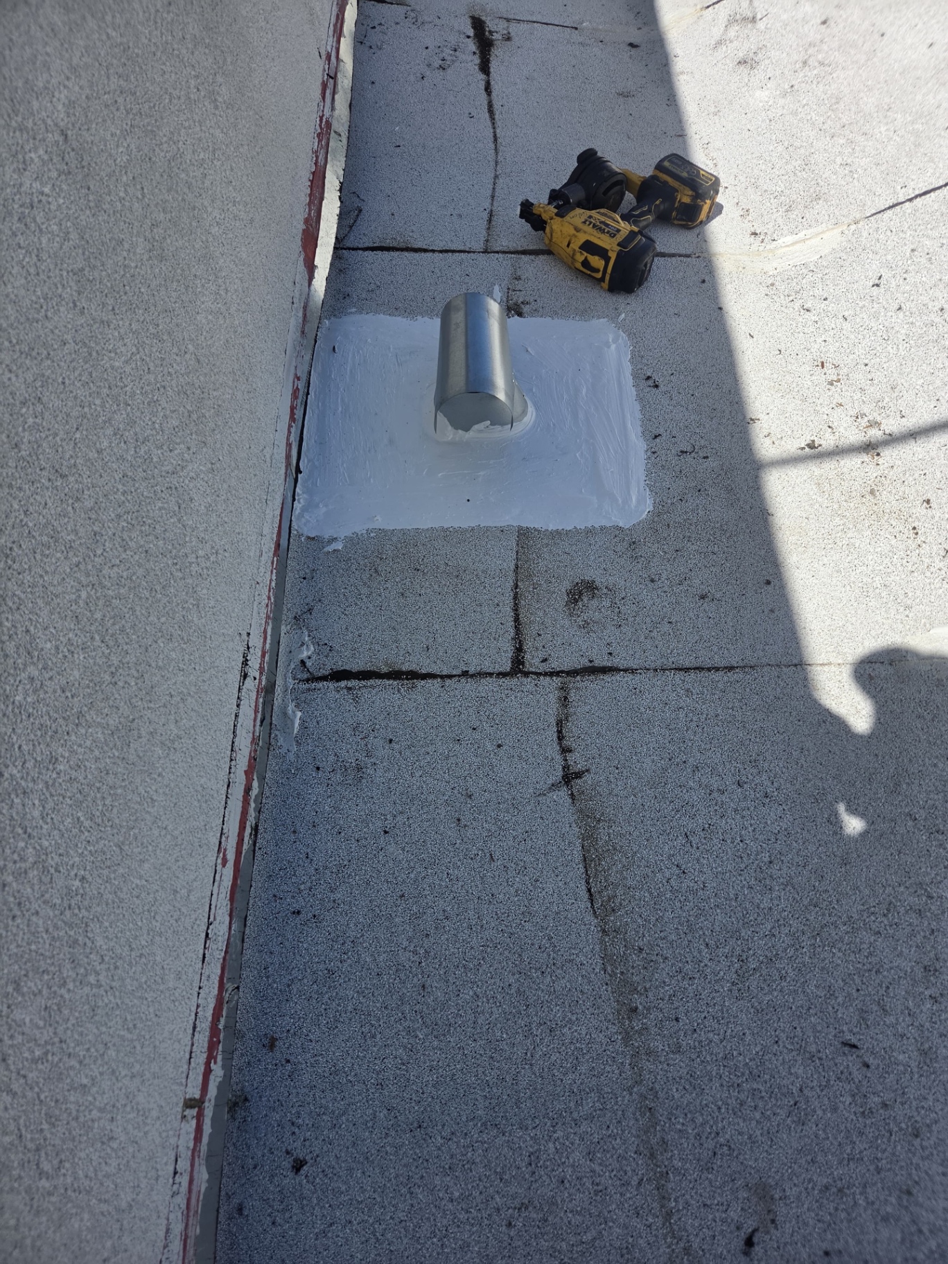Metal vent pipe on a flat roof sealed with white elastomeric flashing cement