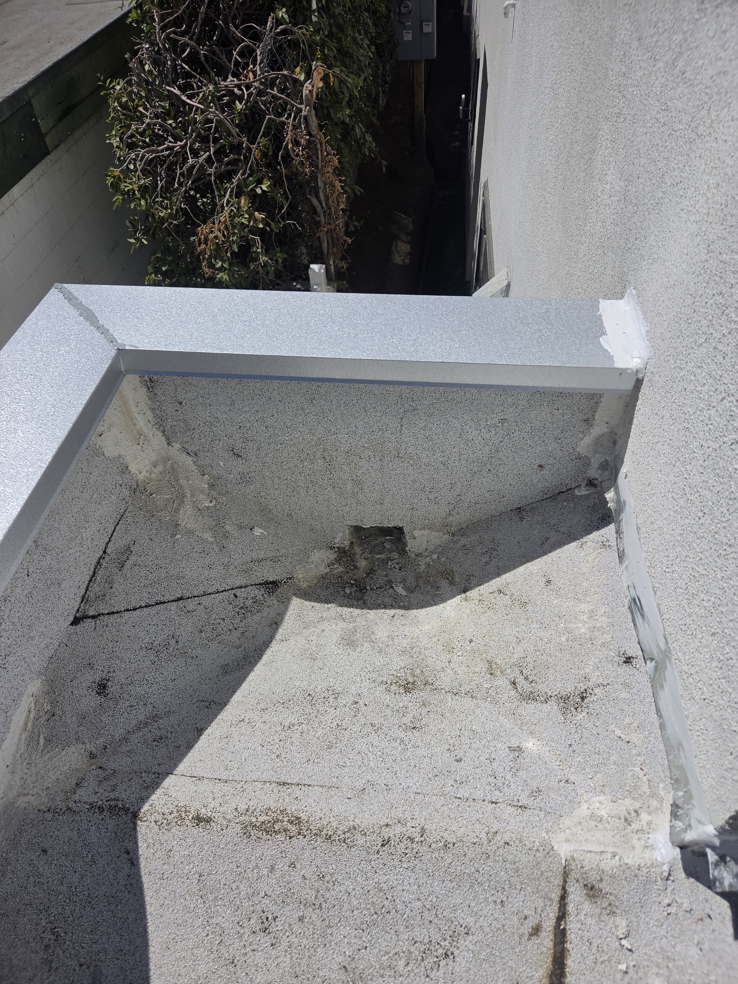 Corner of a flat roof parapet with fresh coping metal and a flashed scupper outlet